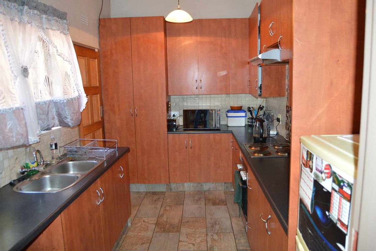 A functional kitchen featuring laminate cabinetry, a double bowl stainless steel sink, built-in oven, electric hob, and tiled flooring.