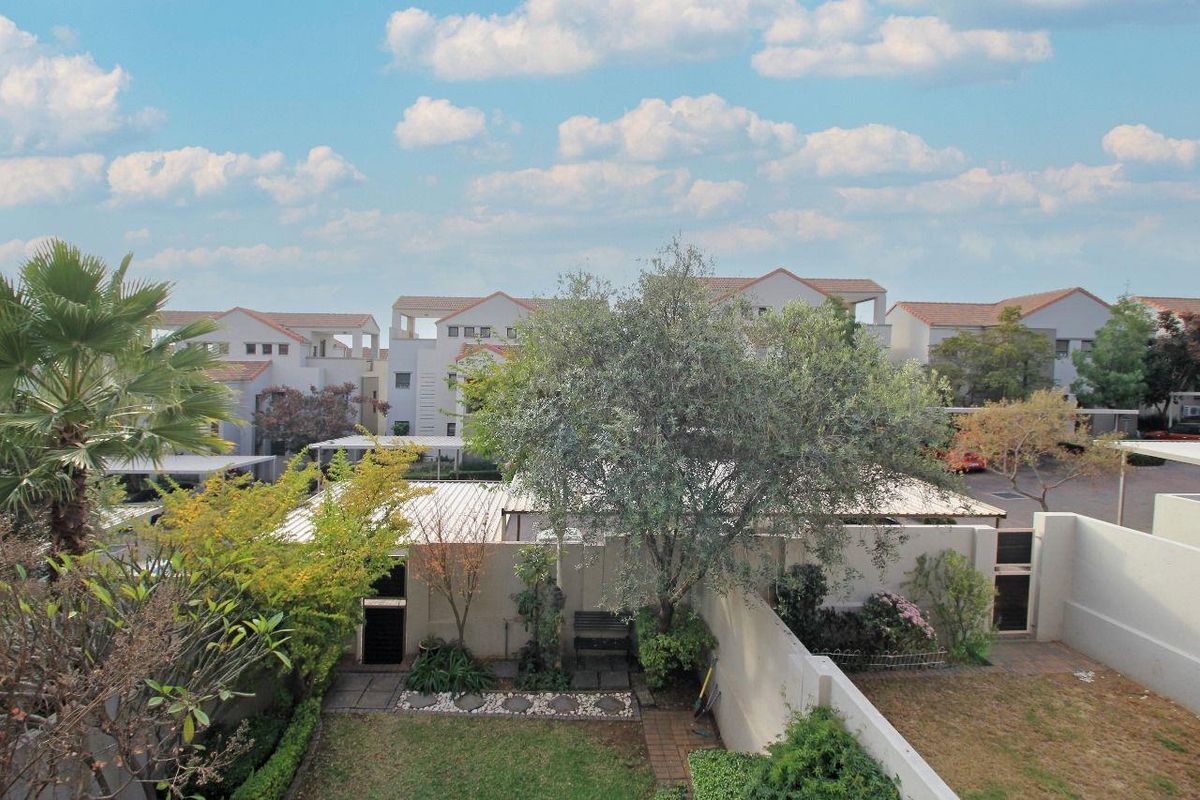 An elevated view of a private townhouse garden featuring established trees, paved pathways, and surrounding residential complex architecture.
