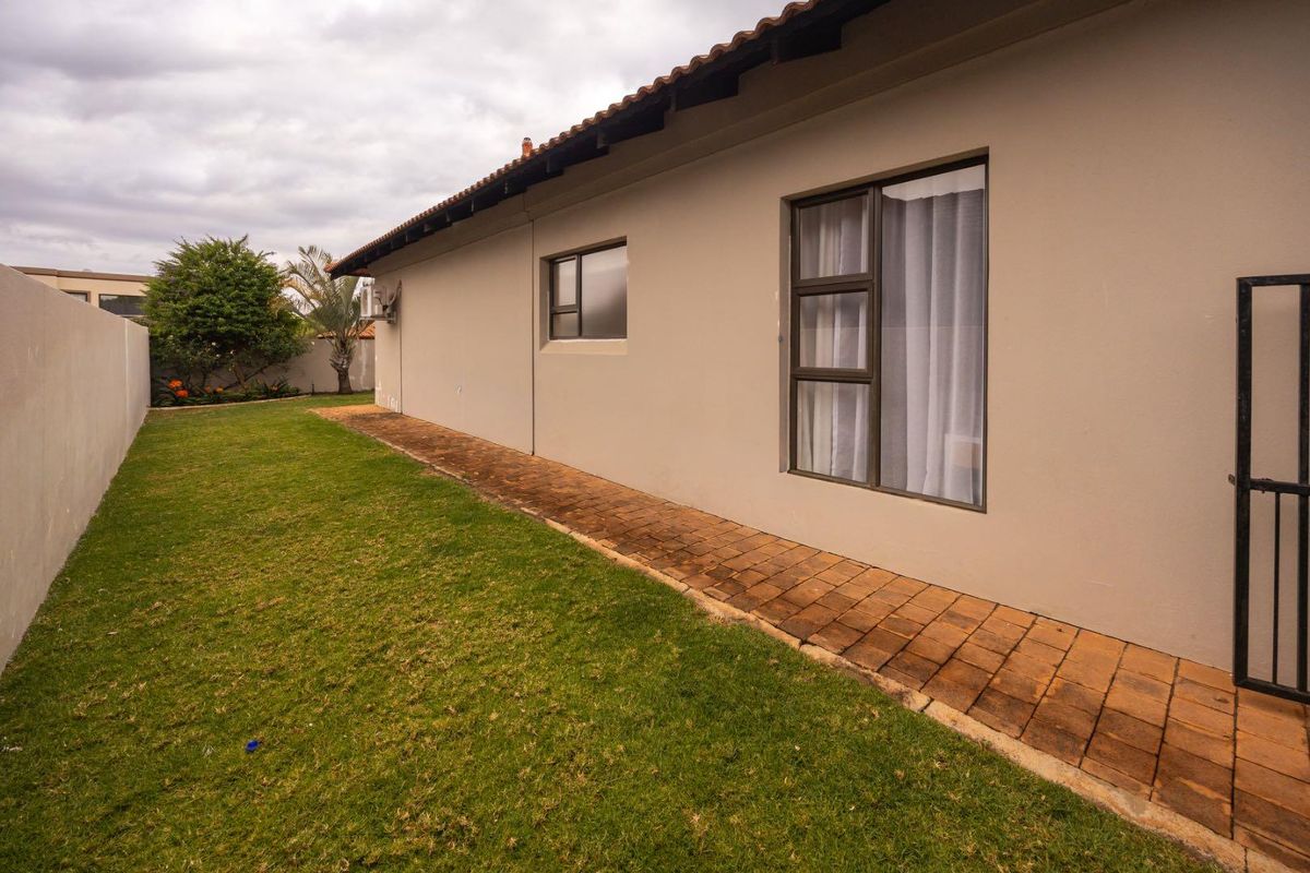 Rear exterior view of the property featuring a brick paved walkway, lawn area, and boundary wall.