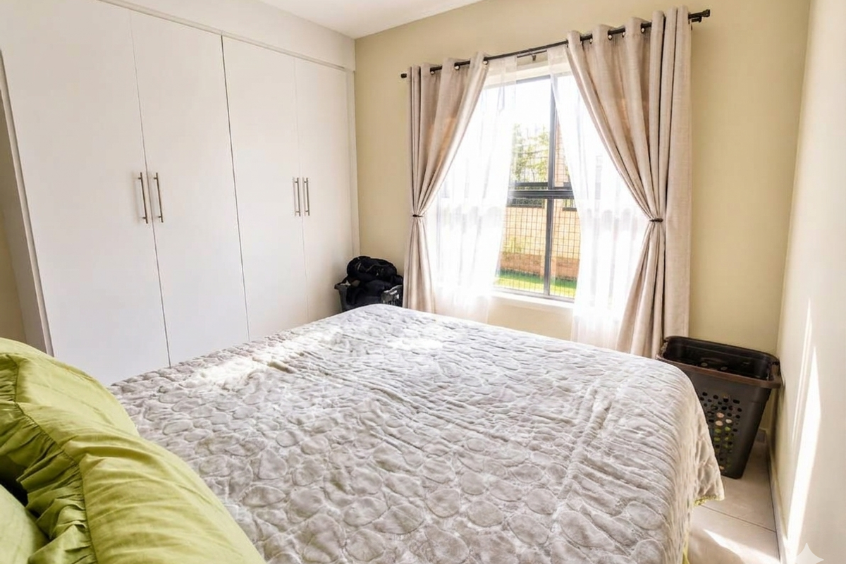 A well-lit bedroom featuring floor-to-ceiling built-in cupboards and a window fitted with security bars.