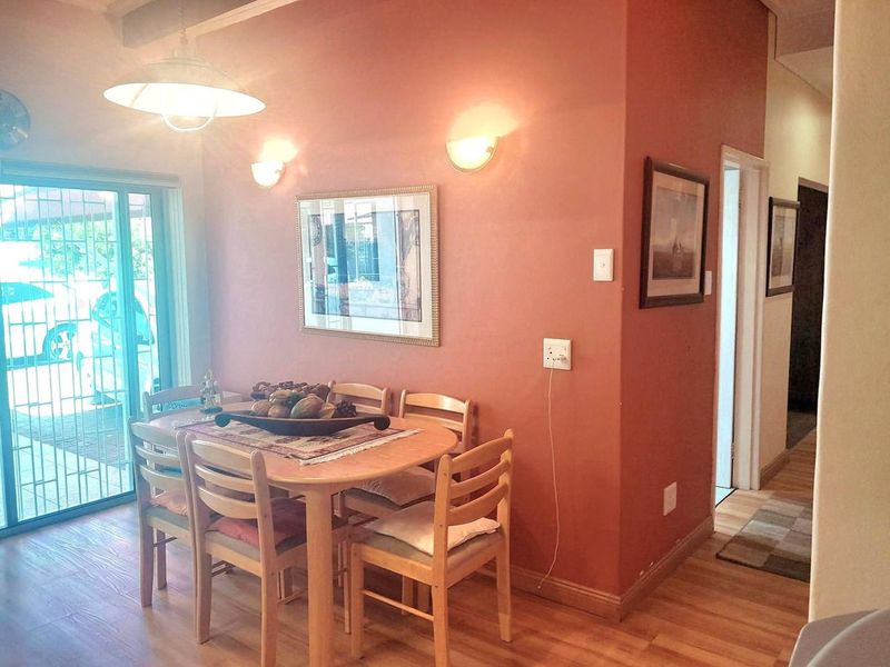 A dining area featuring laminate flooring, wall sconces, and a sliding glass door with security gate providing access to the exterior.