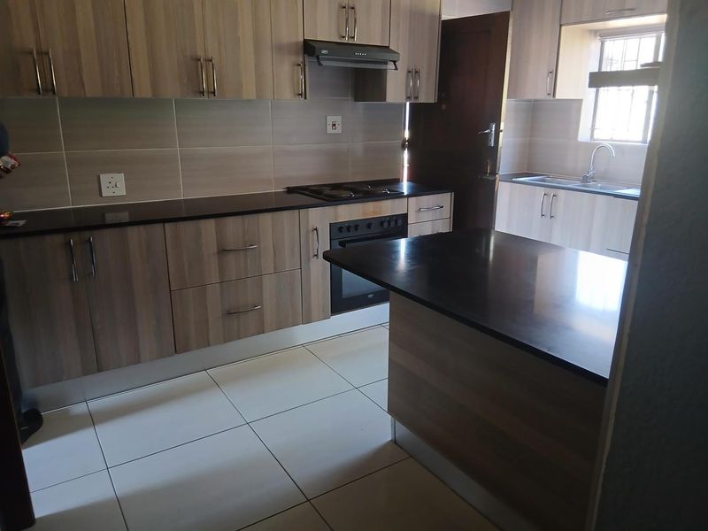 Modern kitchen featuring wood-finish cabinetry, dark granite countertops, built-in oven, hob, extractor fan, and tiled flooring.