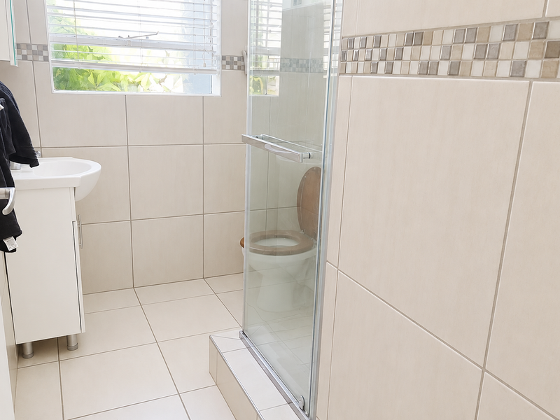 A functional bathroom featuring a vanity cabinet, a glass-enclosed shower, and neutral wall and floor tiling with a decorative mosaic border.