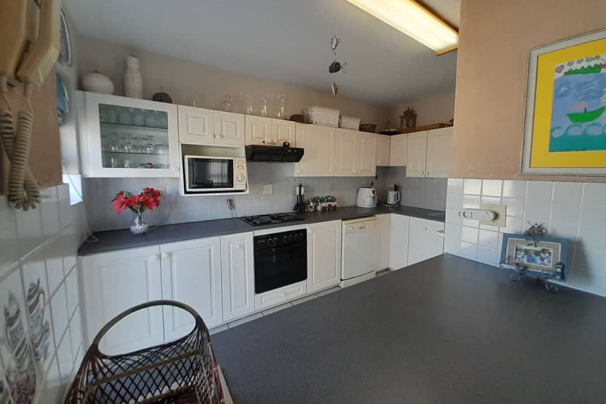 A functional kitchen featuring white cabinetry, dark countertops, a built-in oven, gas hob, extractor fan, and tiled splashbacks.