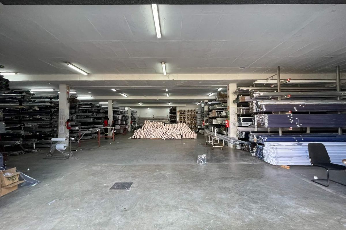 A spacious industrial utility or warehouse area featuring concrete flooring, overhead fluorescent lighting, and structural support columns, currently utilized for storage.