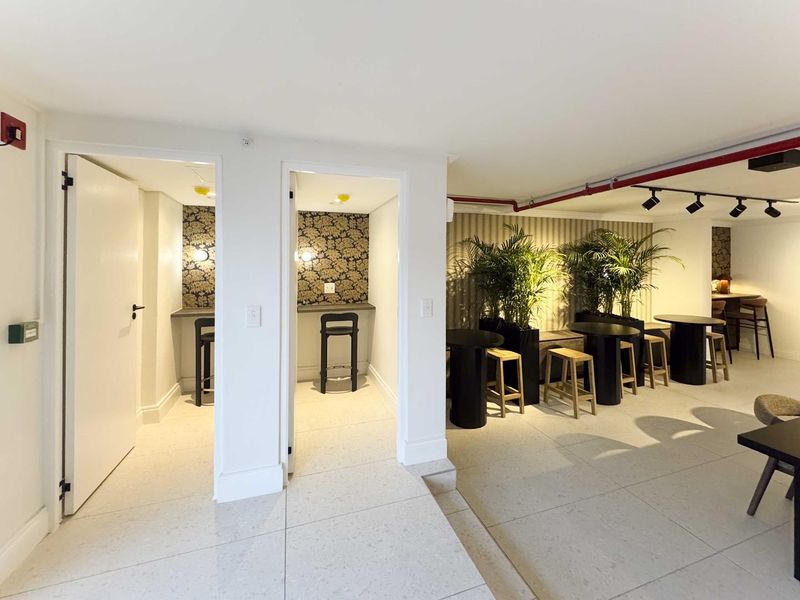 Modern open-plan communal area featuring tiled flooring, track lighting, exposed fire safety infrastructure, and dedicated alcove seating spaces with decorative wallpaper.