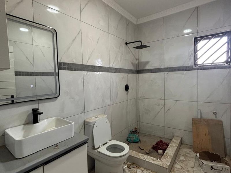 A bathroom featuring modern wall tiles, a vanity with a countertop basin, and a walk-in shower area currently undergoing final finishing and cleaning.