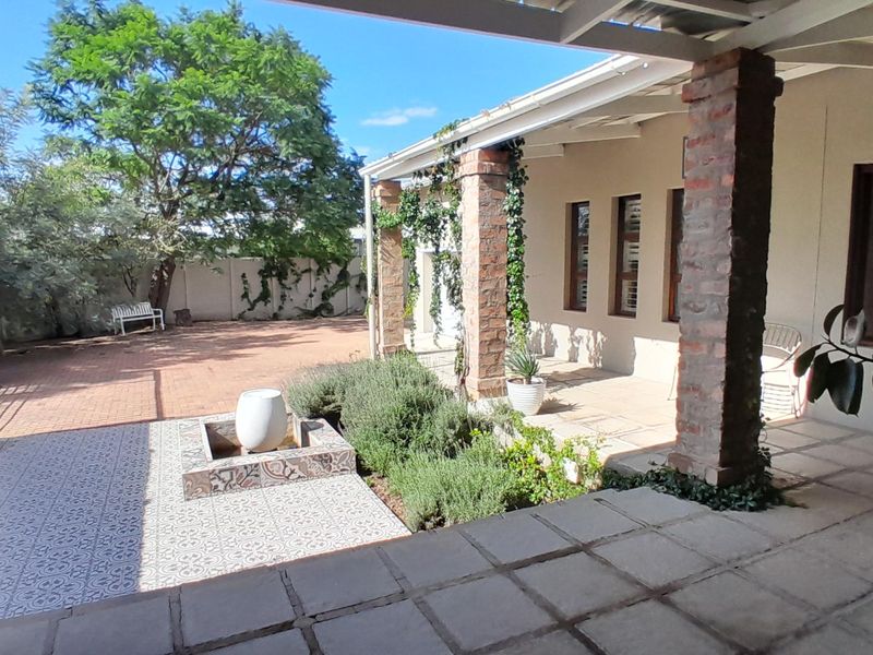 A covered patio area featuring exposed brick pillars, patterned tile accents, and a built-in water feature, overlooking a paved rear garden space.
