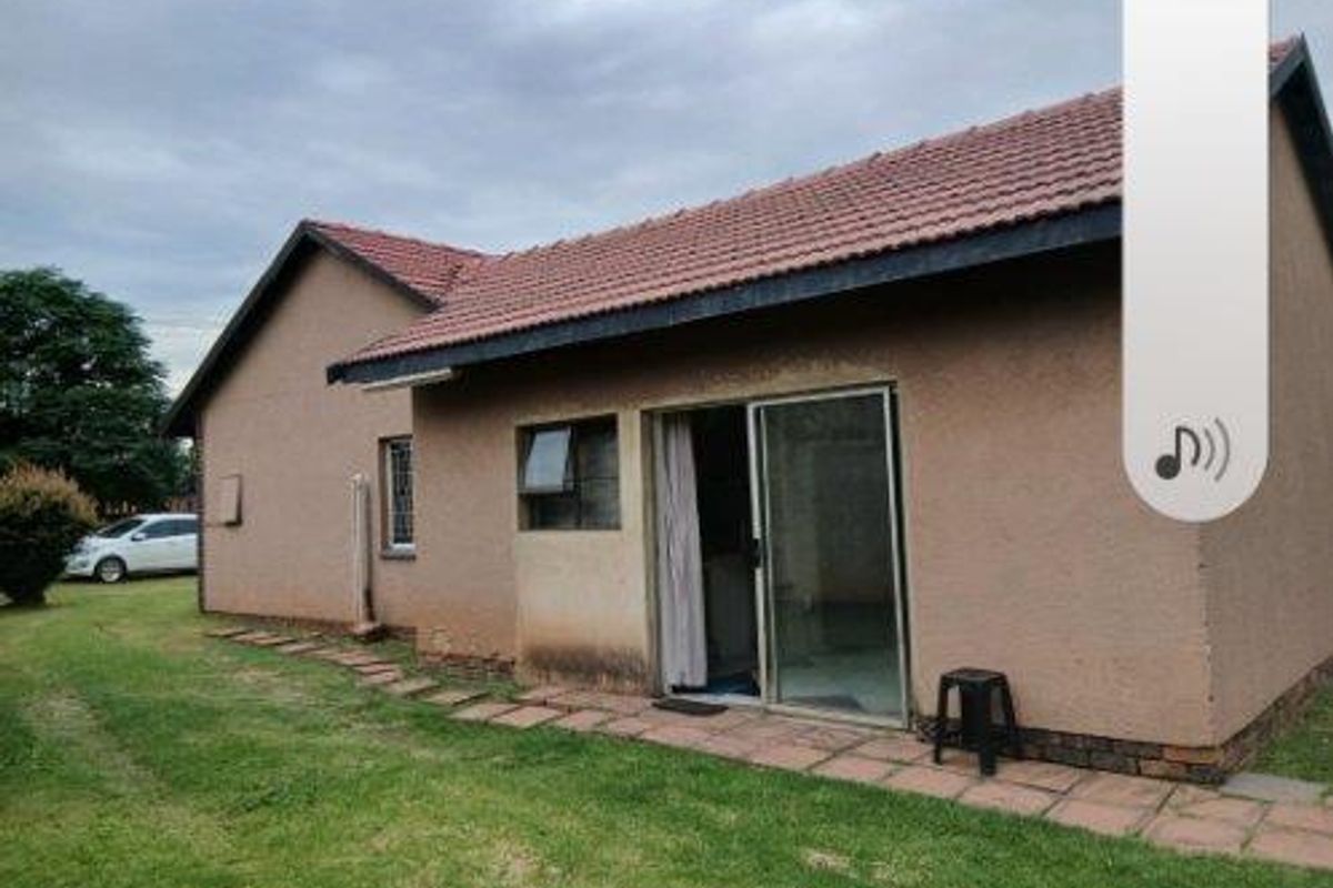 Rear view of a cottage featuring a tiled roof, sliding glass door access, and a paved walkway set within a grassed garden area.