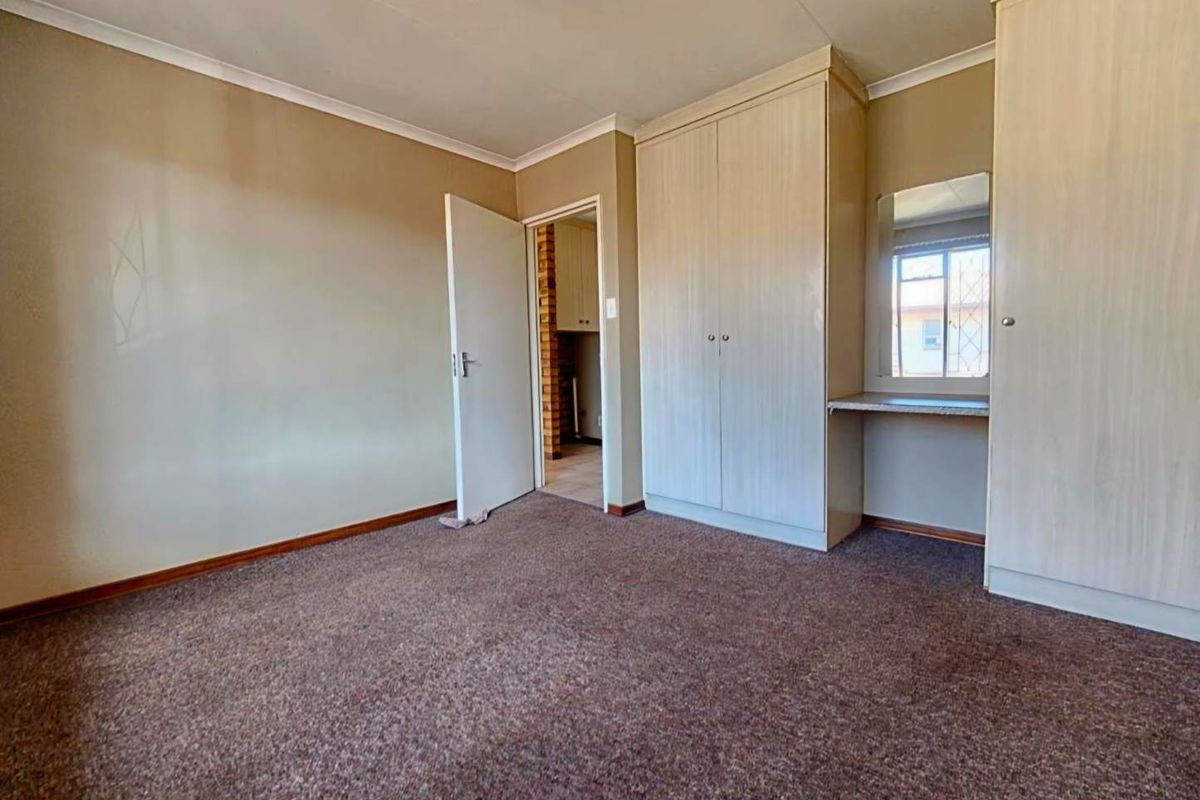 A spacious bedroom featuring neutral walls, carpeted flooring, and extensive built-in cabinetry with an integrated vanity area.