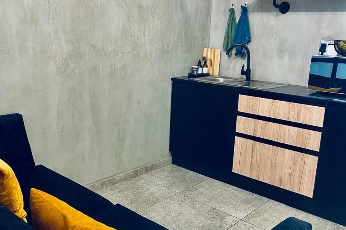 Compact open-plan living area featuring a modern kitchenette with built-in cabinetry, open shelving, and a concrete-effect wall finish.
