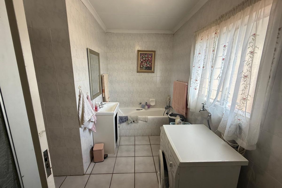A functional bathroom featuring a built-in bathtub, vanity basin, and tiled finishes throughout, with space for laundry appliances.