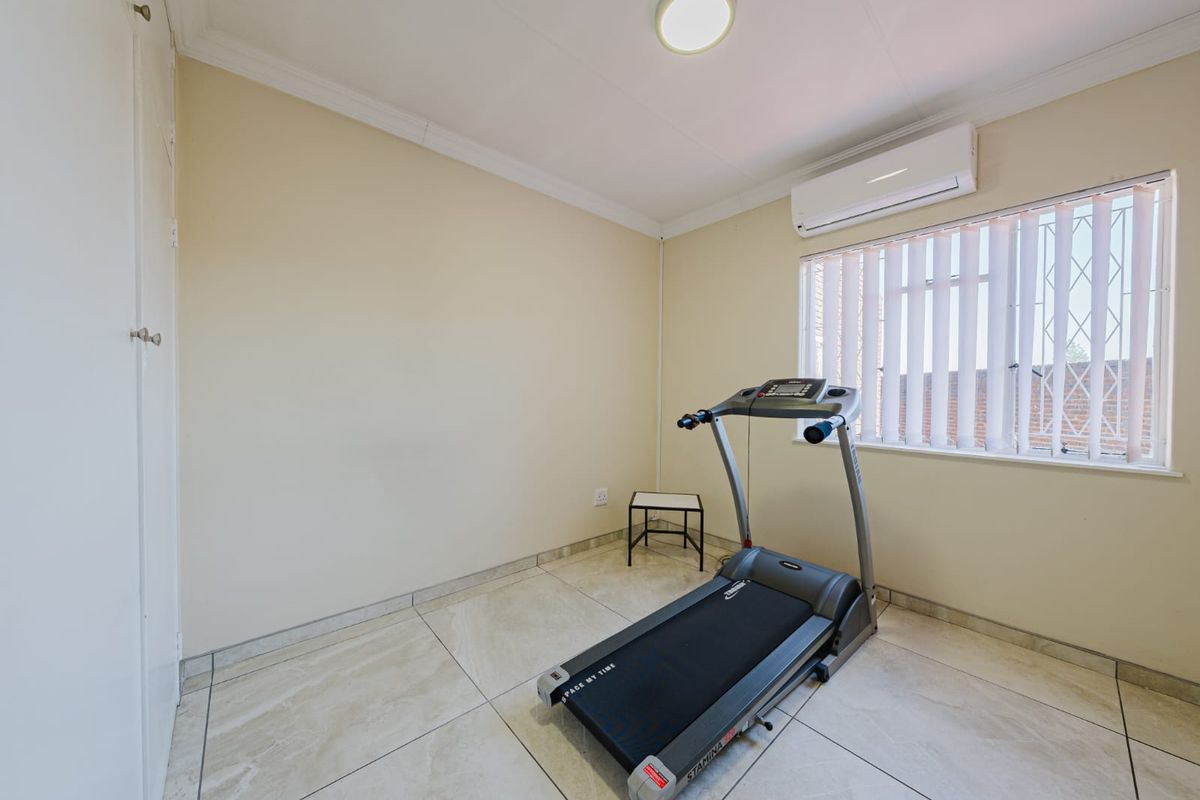A bright bedroom featuring tiled flooring, a built-in cupboard, and an air conditioning unit, with security bars fitted to the window.