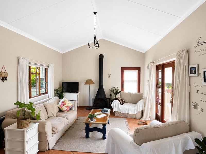 A bright living room featuring a vaulted ceiling, a freestanding fireplace, and terracotta floor tiles, with direct access to the outdoors through glass doors.