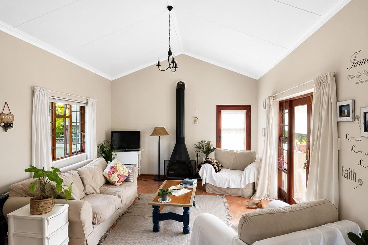 A bright living room featuring a vaulted ceiling, a freestanding fireplace, and terracotta floor tiles, with direct access to the outdoors through glass doors.