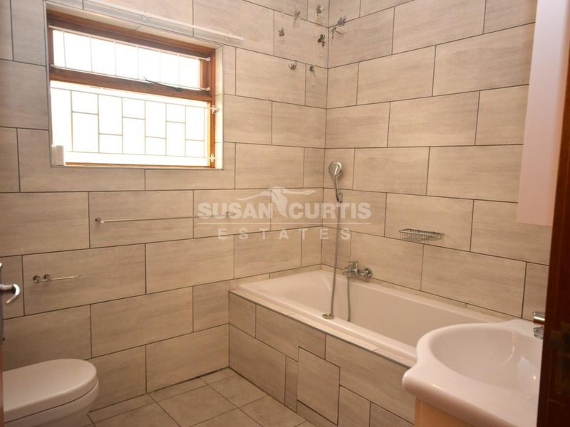 A clean, tiled bathroom featuring a built-in bathtub with shower attachment, pedestal basin, and toilet, finished with neutral wall and floor tiles.