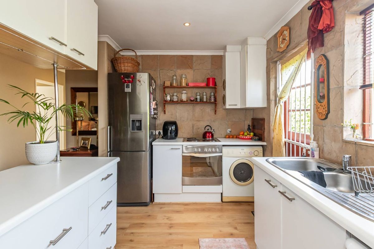 Compact kitchen featuring white cabinetry, stone-look wall tiling, laminate flooring, and integrated appliances including an oven and hob.
