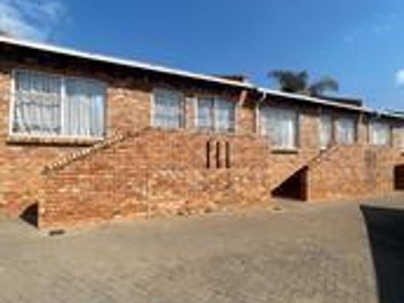 A view of the face-brick exterior facade featuring a paved driveway and multiple window openings.