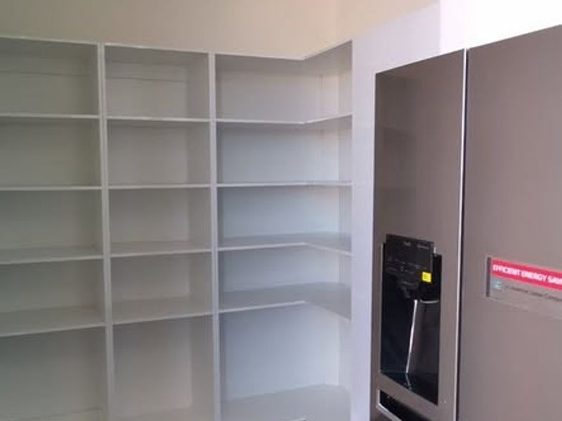 A modern, well-maintained scullery or pantry area featuring extensive built-in shelving, dark marble-look floor tiles, and recessed lighting.