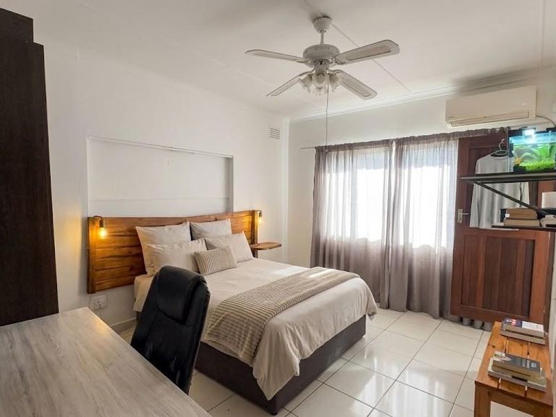 A well-maintained bedroom featuring tiled flooring, a ceiling fan, and a split-system air conditioner for climate control.