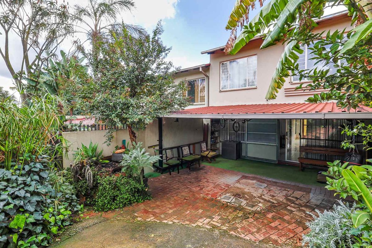 A rear patio area featuring brick paving, a covered roof structure, and established garden landscaping.