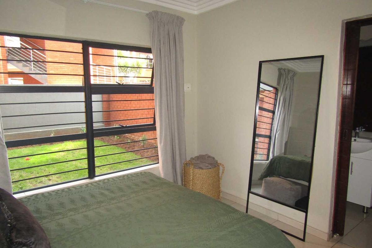 A bedroom featuring tiled flooring, aluminium window frames with security bars, and direct access to an en-suite bathroom.