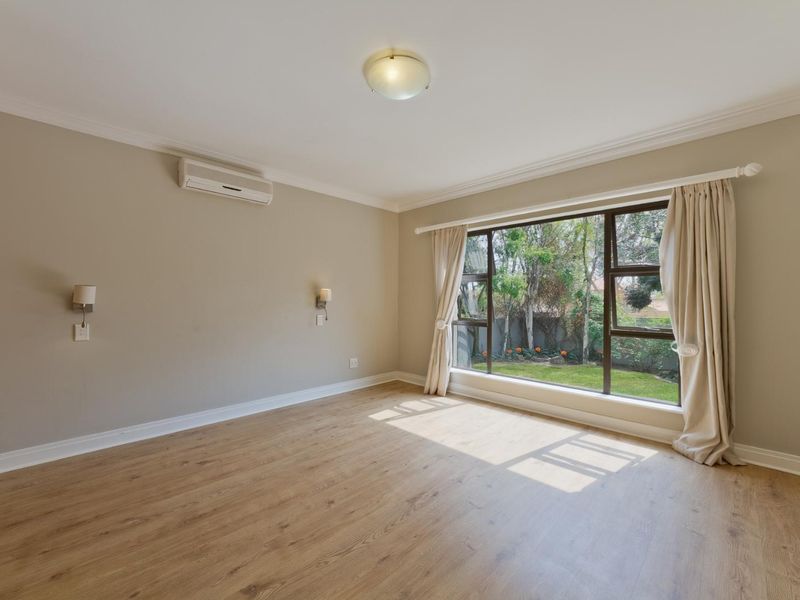 A bright, empty bedroom featuring laminate flooring, an air conditioning unit, and a large window overlooking the garden.