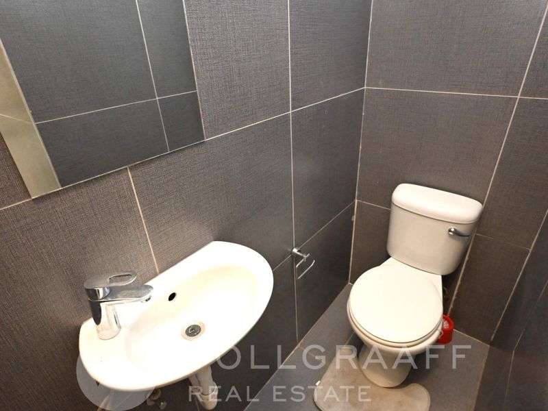 A compact guest bathroom featuring modern grey wall tiles, a wall-mounted basin with chrome tapware, and a standard toilet.