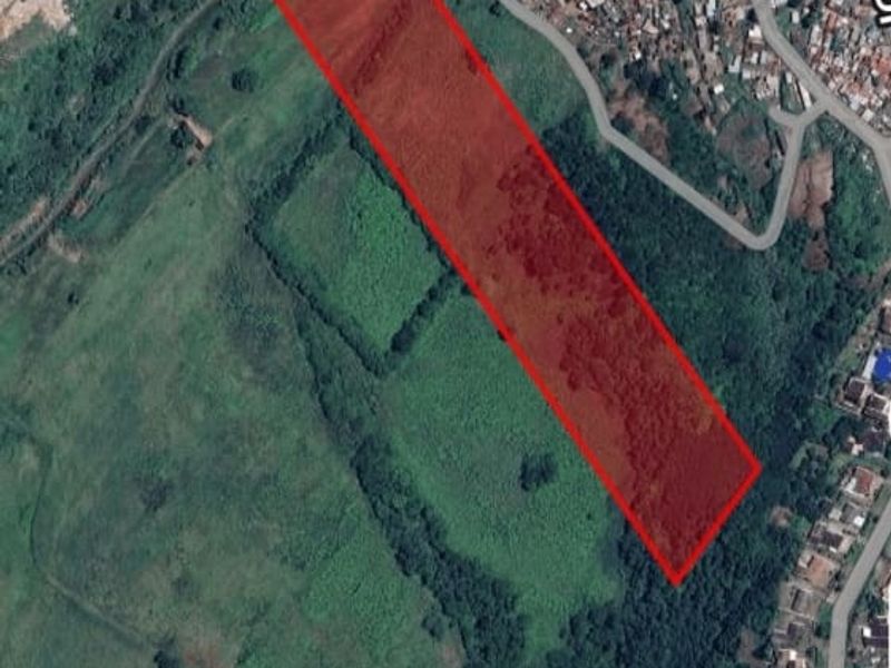An aerial satellite view showing a large, undeveloped plot of land highlighted in red, situated within a residential area.