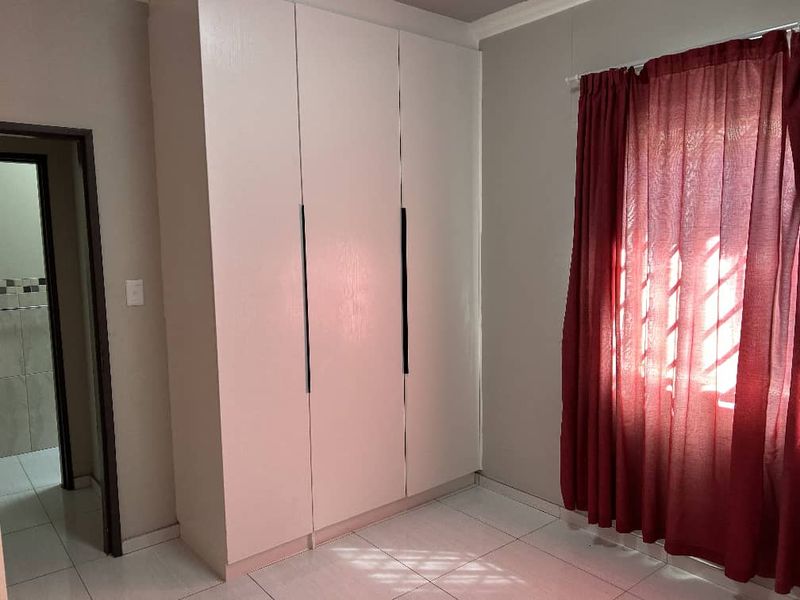 A clean, empty bedroom featuring neutral tiled flooring and a large built-in wardrobe with modern handles.