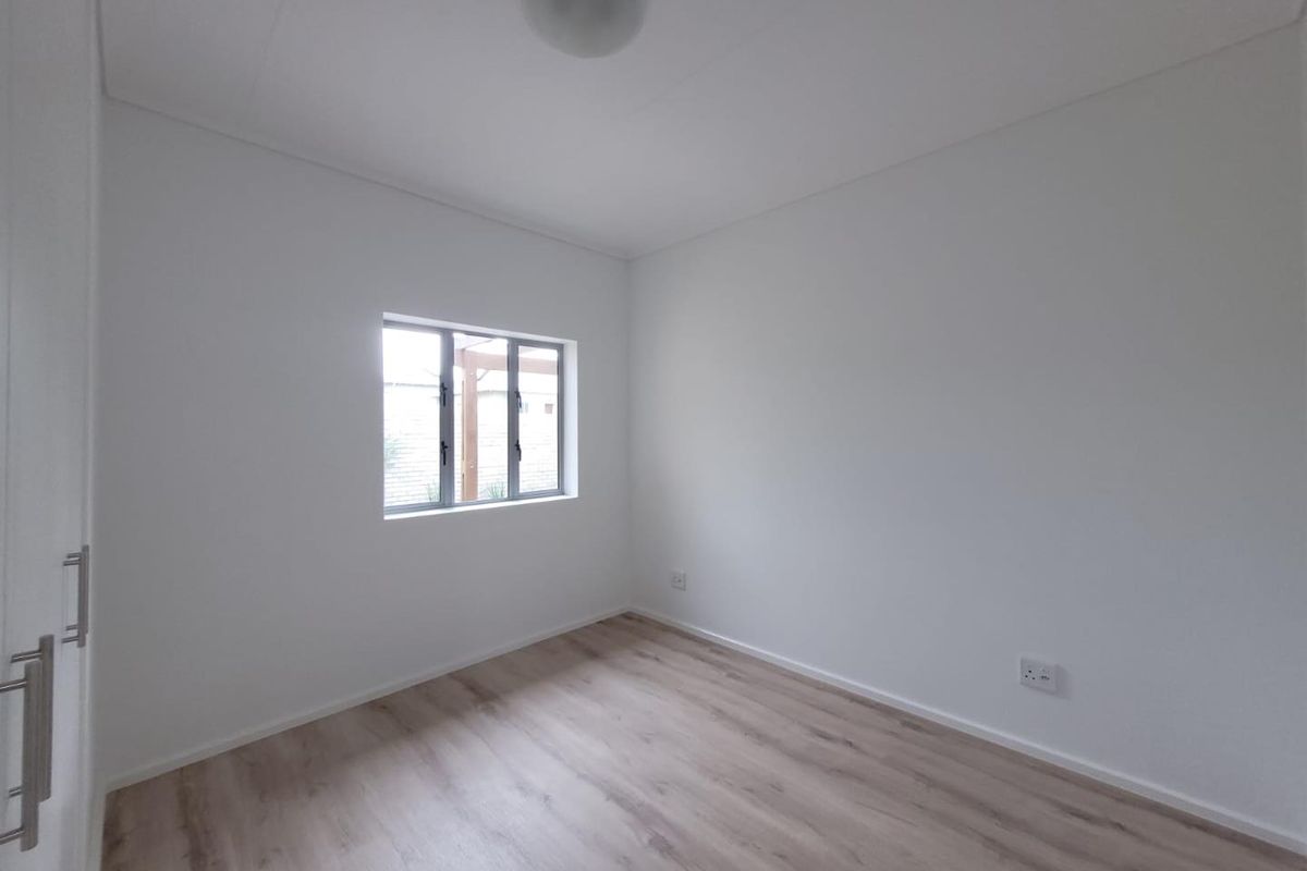 A bright, empty bedroom featuring light wood-look laminate flooring, neutral white walls, and a built-in wardrobe.