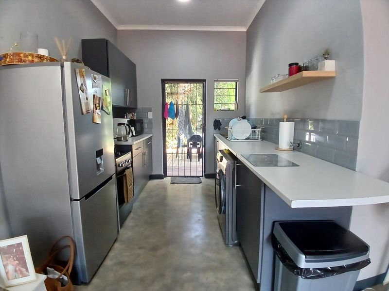 A functional galley-style kitchen featuring modern grey cabinetry, subway tile backsplash, concrete flooring, and direct access to the rear outdoor area.