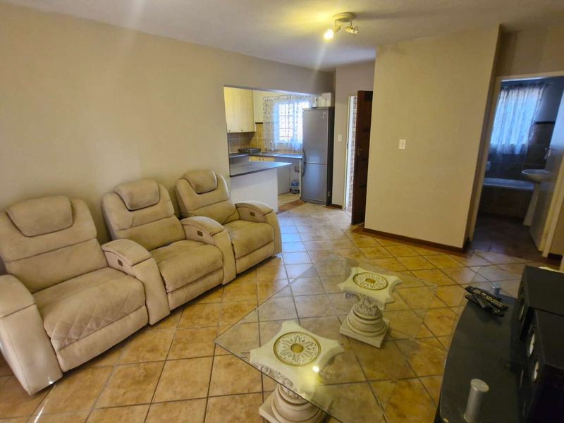 Open plan living area featuring tiled flooring, with a view into the kitchen and an adjacent bathroom.