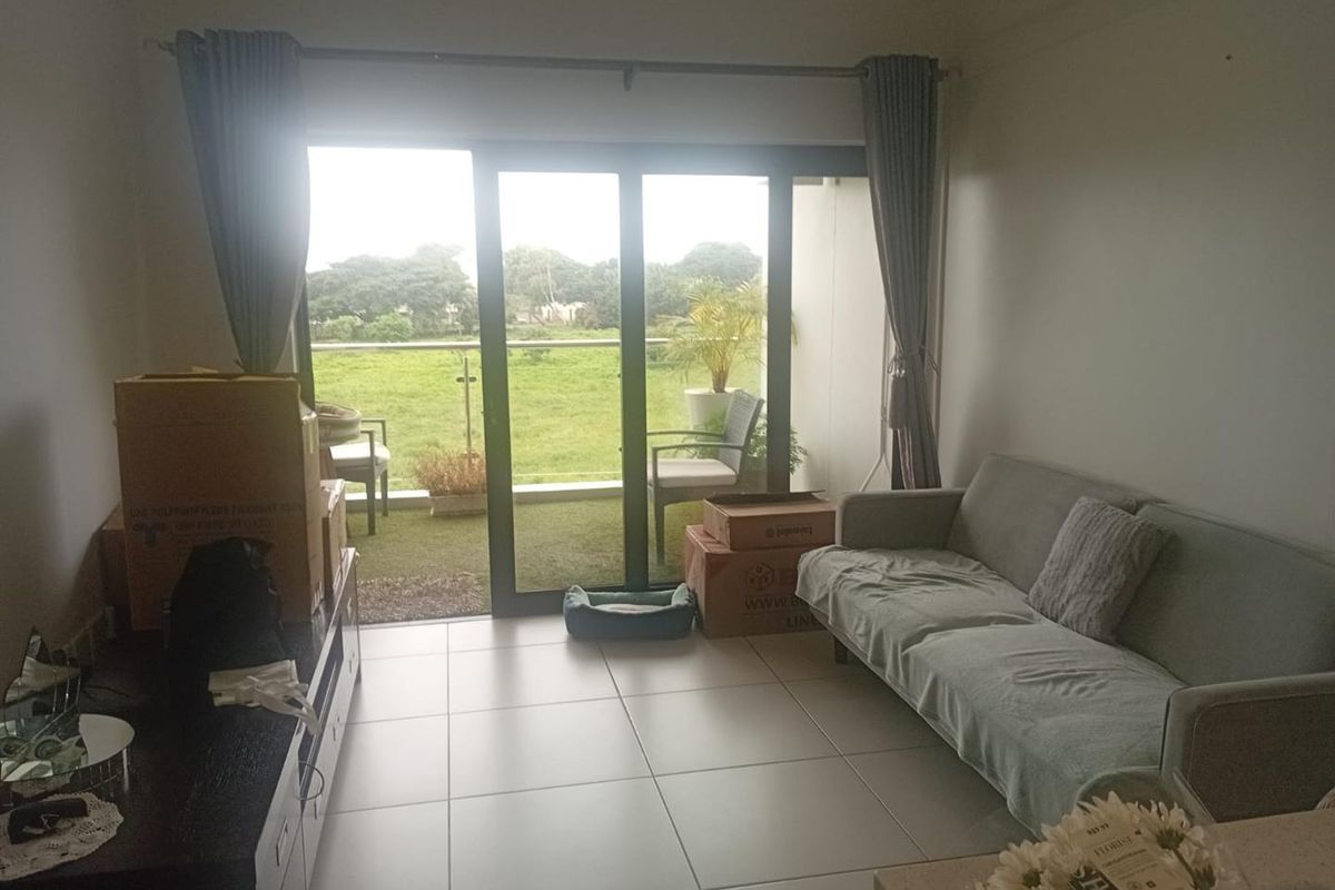 A living room featuring large sliding glass doors that open onto a balcony with green views, finished with neutral floor tiles.