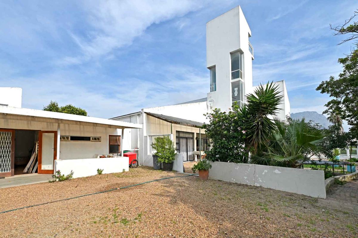 Rear view of a multi-level architectural home featuring a distinctive tower structure, gravel courtyard, and covered patio area.