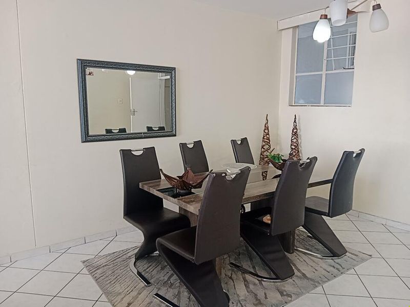 A functional dining room featuring tiled flooring, neutral walls, and a window with security bars, providing a bright and practical space for meals.