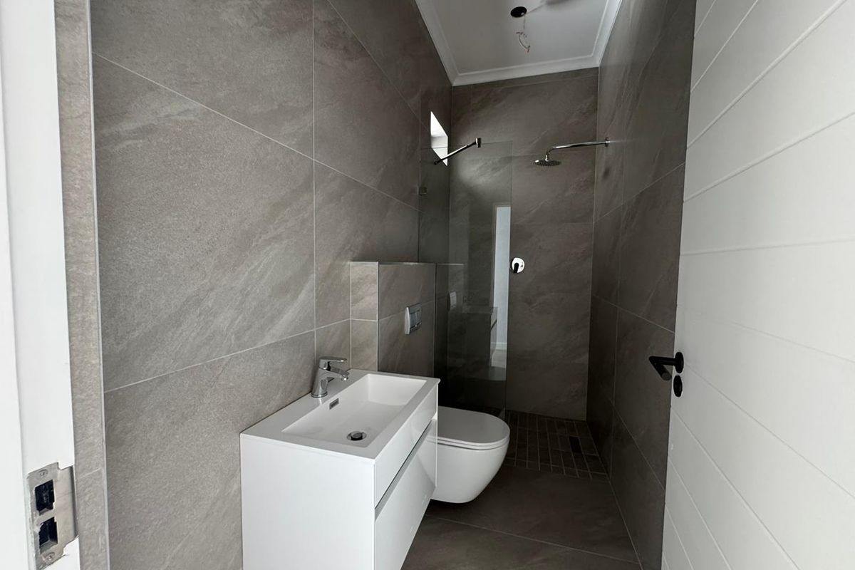 Modern bathroom featuring large-format grey floor-to-ceiling tiles, a wall-mounted vanity, a floating toilet, and a walk-in shower with a glass screen.