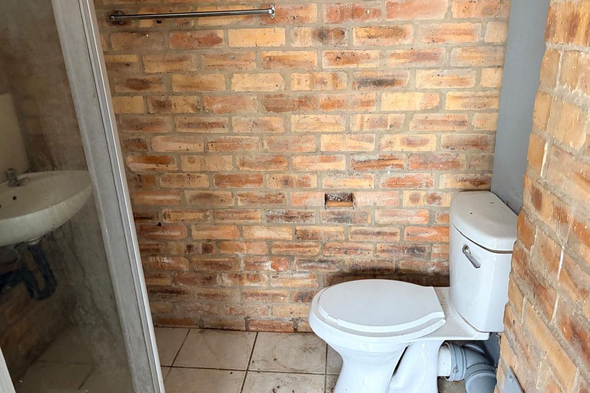 A bathroom featuring an exposed brick wall, a standard toilet, and a basin, requiring some maintenance and cosmetic updates.