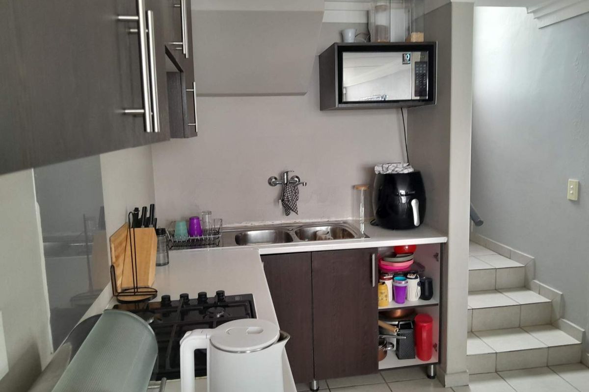 Compact kitchen area featuring dark cabinetry, a built-in gas hob, double stainless steel sink, and an integrated microwave shelf.