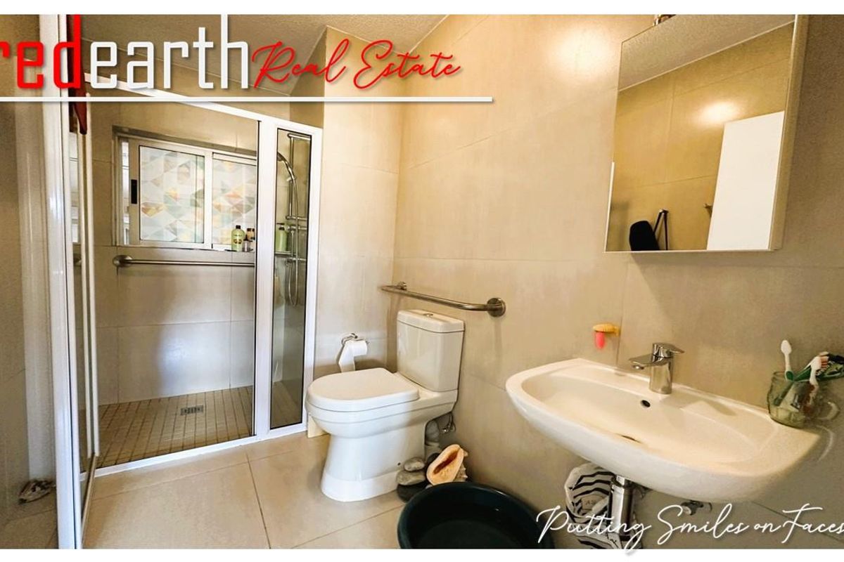A functional bathroom featuring a walk-in shower with safety grab rails, a wall-mounted basin, and a standard toilet.