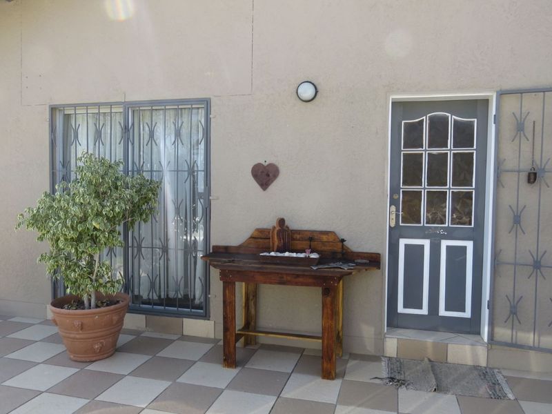 A paved patio area featuring a sliding glass door with security bars and a single entry door with decorative glass panels.