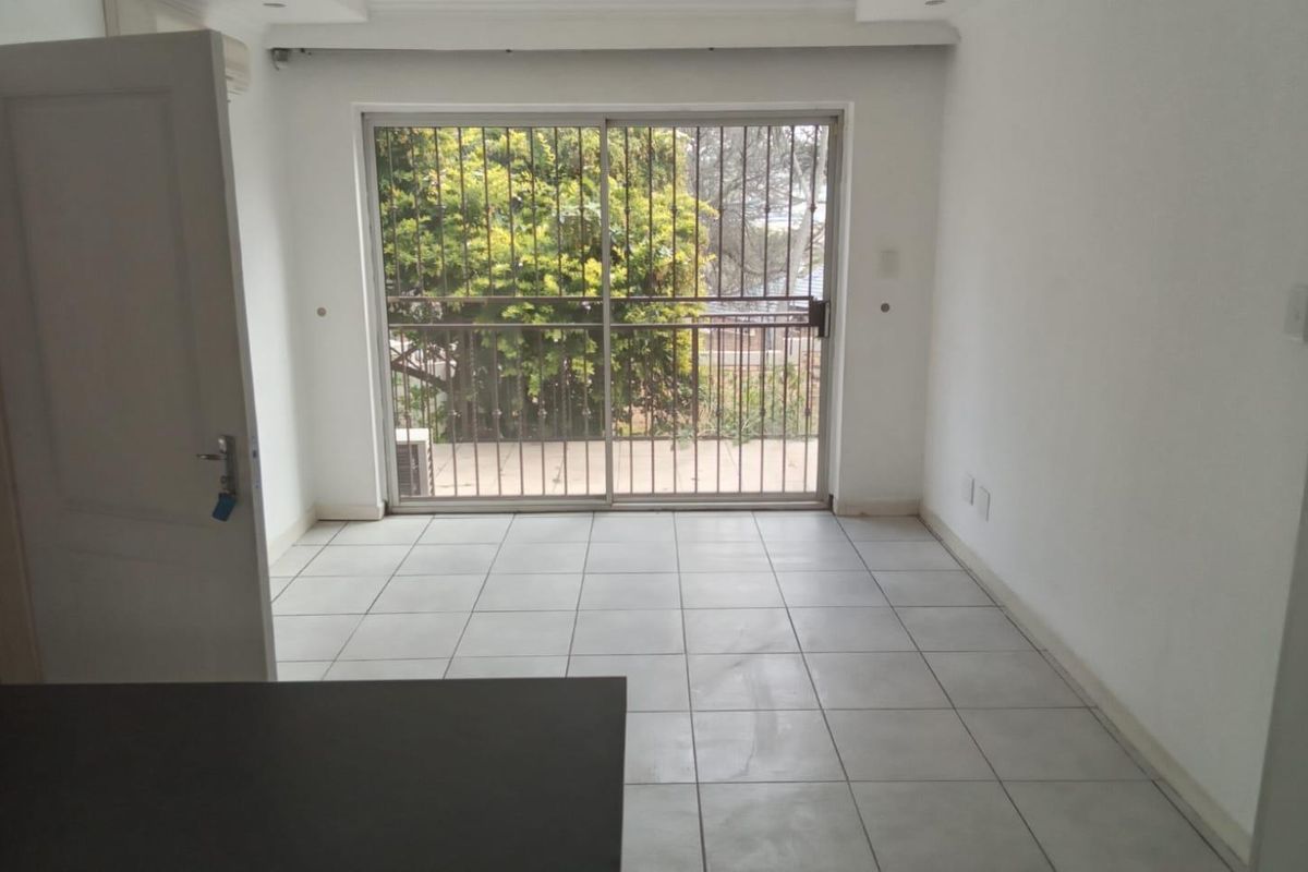 A bright, empty living area featuring neutral floor tiles and a large sliding glass door with security bars leading to an outdoor space.