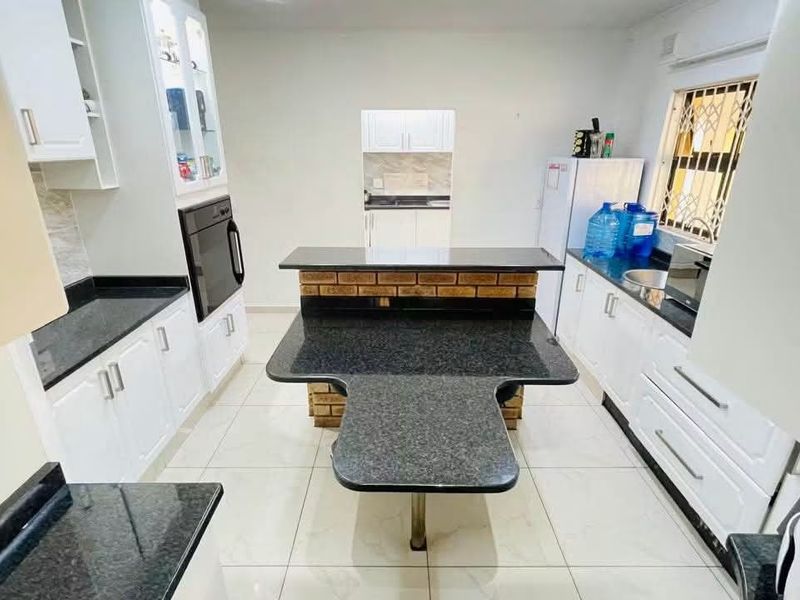 A functional kitchen featuring white cabinetry, dark granite countertops, a central island with breakfast bar, and tiled flooring.