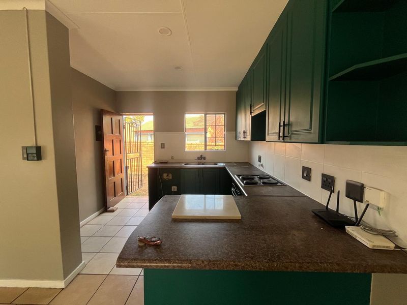 A functional kitchen featuring dark green cabinetry, laminate countertops, a built-in hob, and tiled flooring with direct access to an outdoor area.
