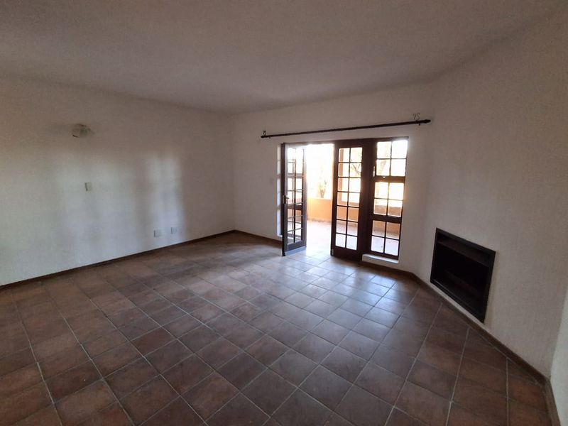 Spacious living room featuring terracotta-style tiled flooring, a built-in fireplace, and direct access to an outdoor area through classic french doors.