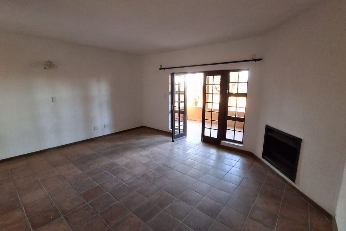 Spacious living room featuring terracotta-style tiled flooring, a built-in fireplace, and direct access to an outdoor area through classic french doors.