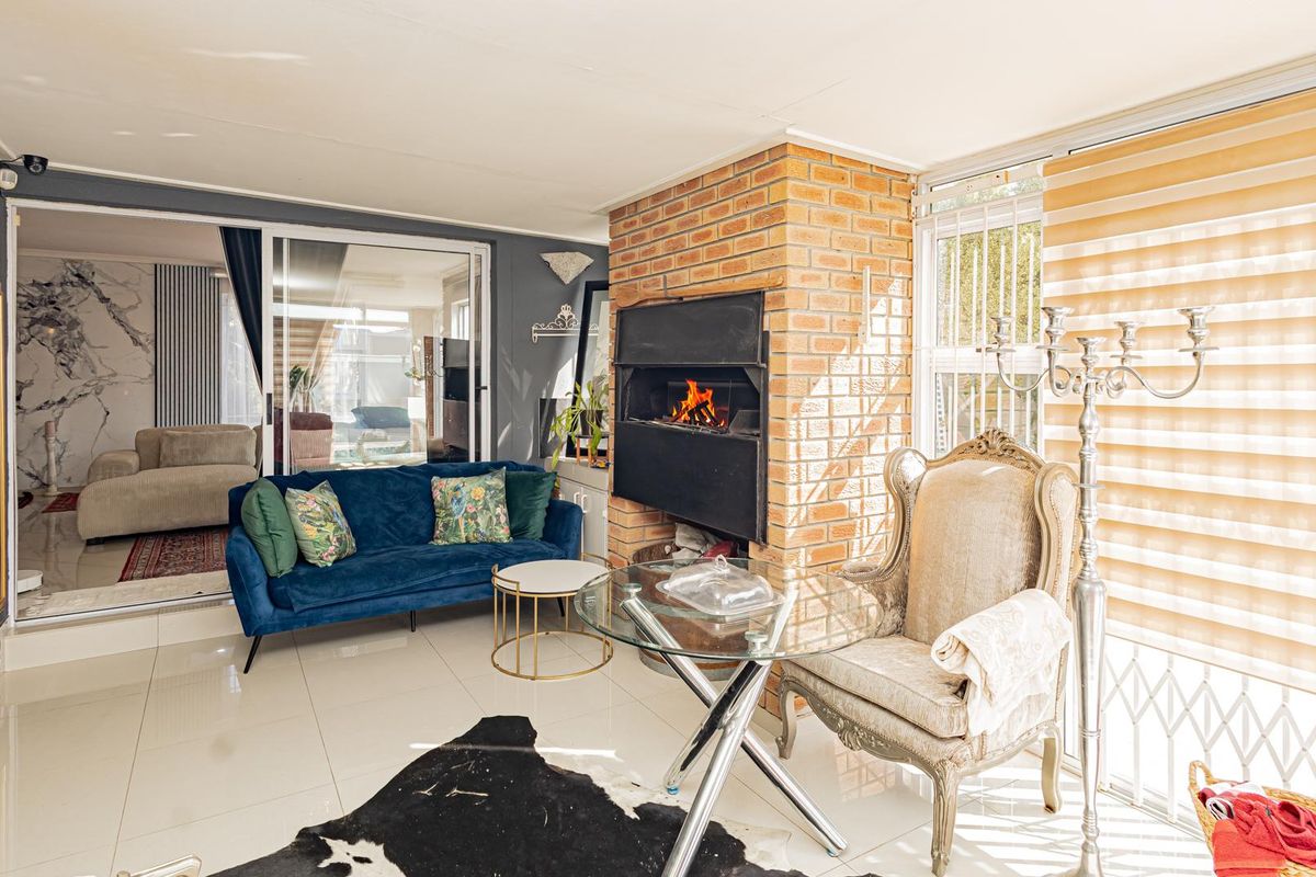 A bright living room featuring a prominent brick fireplace, large sliding glass doors, and polished tile flooring, offering a cozy and well-lit space.