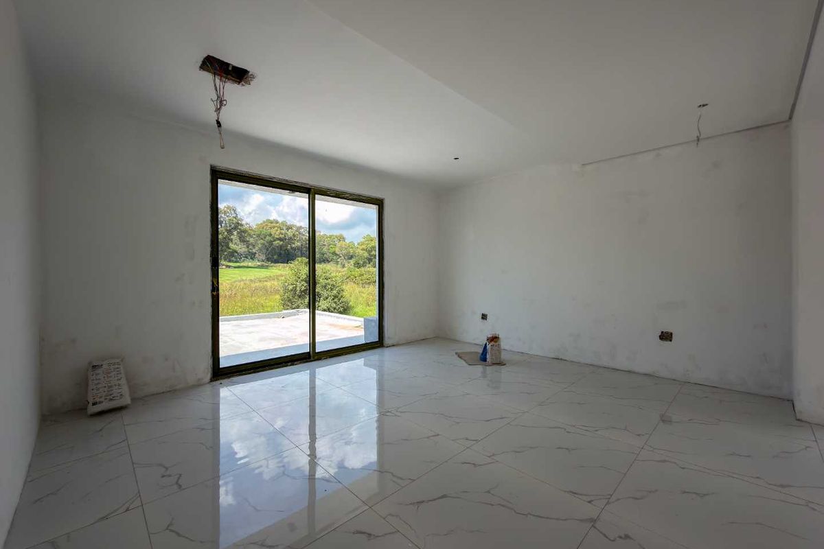 An empty, unfinished living area featuring large format marble-look floor tiles and a sliding glass door leading to an outdoor patio.