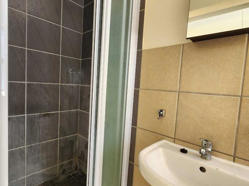 A functional bathroom featuring a shower enclosure with tiled walls and a pedestal basin with a wall-mounted mirror.