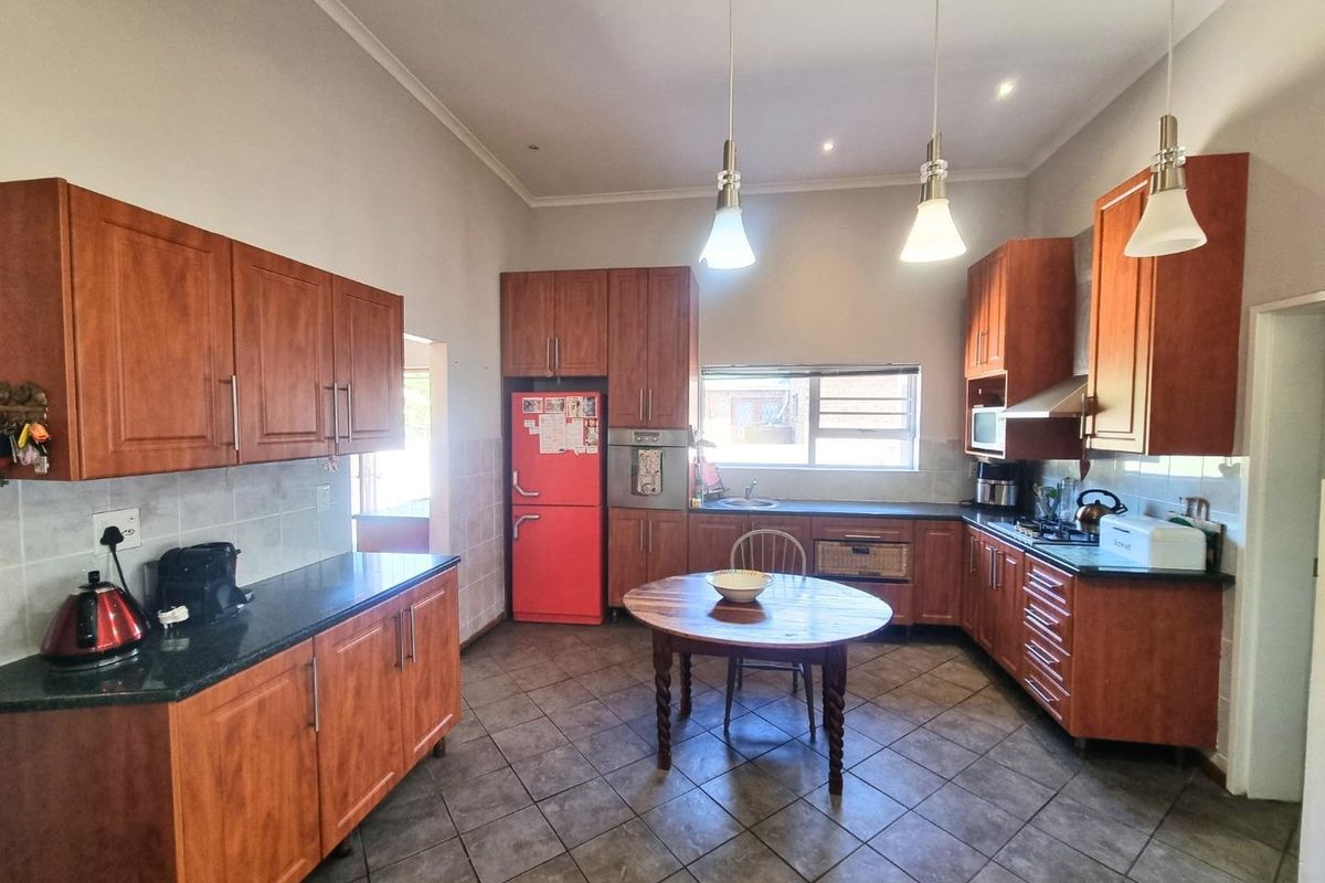 Spacious kitchen featuring wood-finish cabinetry, dark countertops, integrated oven, gas hob, extractor fan, and tiled flooring with a central dining area.